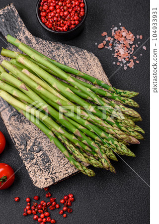 Delicious fresh sprigs of asparagus on a dark textured background Delicious fresh sprigs of asparagus on a dark textured background 104933931