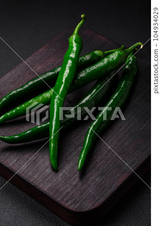 Fresh hot green chili peppers on a dark concrete background Fresh hot green chili peppers on a dark concrete background 104934029