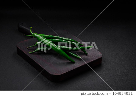 Fresh hot green chili peppers on a dark concrete background Fresh hot green chili peppers on a dark concrete background 104934031