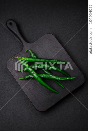 Fresh hot green chili peppers on a dark concrete background Fresh hot green chili peppers on a dark concrete background 104934032