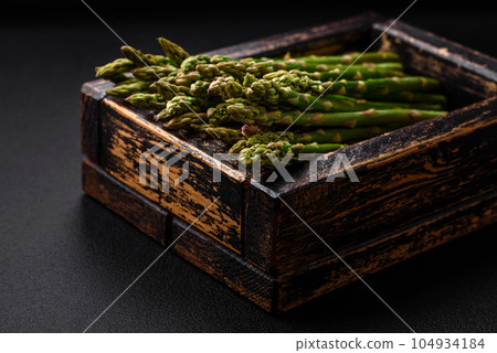Delicious fresh sprigs of asparagus on a dark textured background Delicious fresh sprigs of asparagus on a dark textured background 104934184