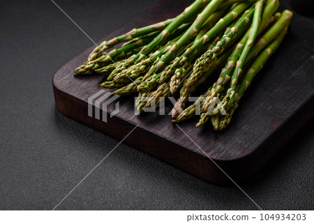 Delicious fresh sprigs of asparagus on a dark textured background Delicious fresh sprigs of asparagus on a dark textured background 104934203