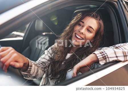 Portrait of a beautiful smiling woman in a car looking out of the window 104934825
