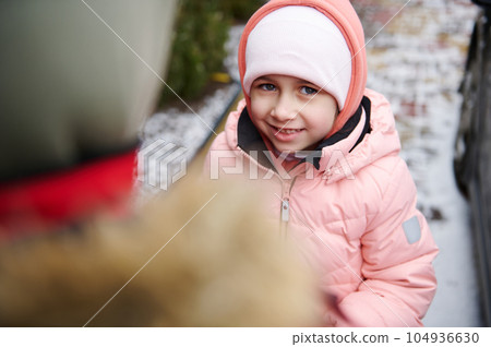 Caucasian lovely little child girl smiling looking at camera, standing near her older brother in a snow covered backyard 104936630
