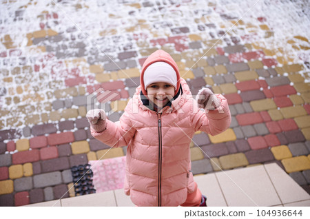 Smiling happy child girl in pink warm down jacket, smiling at camera, standing on stairs in the porch of a mansion Smiling happy child girl in pink warm down jacket, smiling at camera, standing on stairs in the porch of a mansion 104936644
