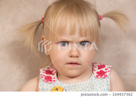 Portrait of a 2-year-old girl frowning suspiciously looking at the camera. Portrait of a 2-year-old girl frowning suspiciously looking at the camera. 104937362