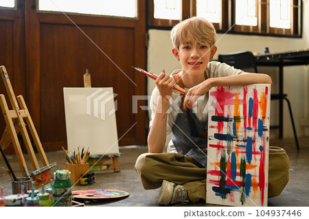 Smiling Asian student man painting on canvas with watercolors at art class. Art, education, creativity and people concept 104937446