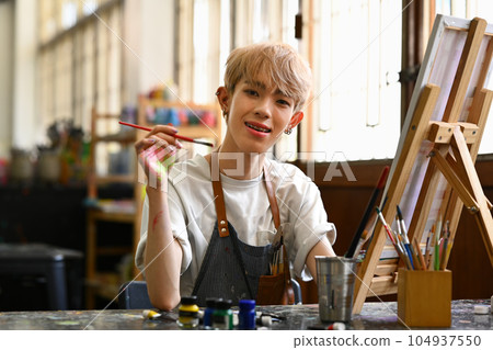 Smiling Asian student man painting on canvas with watercolors at art class. Art, education, creativity and people concept 104937550