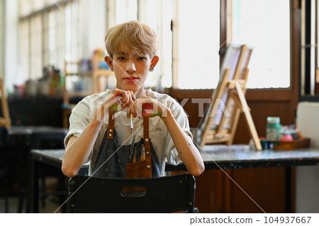 Smiling Asian student man painting on canvas with watercolors at art class. Art, education, creativity and people concept Smiling Asian student man painting on canvas with watercolors at art class. Art, education, creativity and people concept 104937667