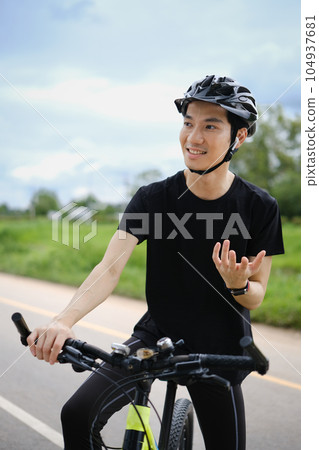 Happy asian man cyclist speaking on phone through earphones while having break during cycling bike in the park 104937681