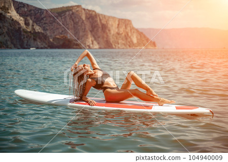 Woman sup sea. Sports girl on a surfboard in the sea on a sunny summer day. In a black bathing suit, he sits on a sapa in the sea. Rest on the sea. Woman sup sea. Sports girl on a surfboard in the sea on a sunny summer day. In a black bathing suit, he sits on a sapa in the sea. Rest on the sea. 104940009