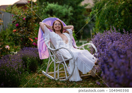 Woman sits on the vintage chair in the garden white dress 104940398
