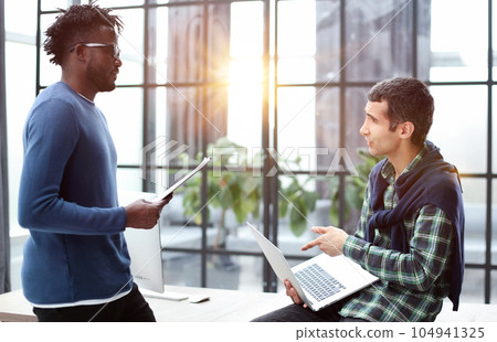 Two cheerful businessmen discussing something on the laptop in an office Two cheerful businessmen discussing something on the laptop in an office 104941325
