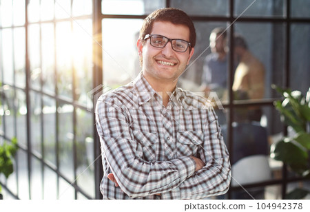 Young businessman with arms crossed standing in office lobby Young businessman with arms crossed standing in office lobby 104942378