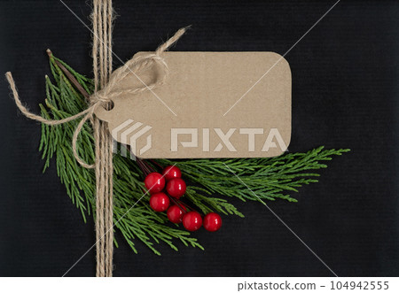Blank brown craft gift tag with rope, cedar tree branches and berries on black background. Mockup, copy space, close up Blank brown craft gift tag with rope, cedar tree branches and berries on black background. Mockup, copy space, close up 104942555