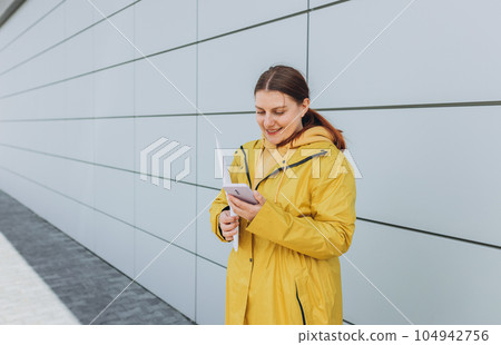 Young woman in yellow uniform using smartphone and holding package. Delivery service holding to sent a white package letter, for mockup Young woman in yellow uniform using smartphone and holding package. Delivery service holding to sent a white package letter, for mockup 104942756