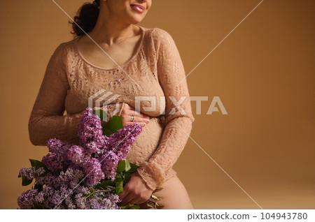 Close-up. Bunch of lilac flowers in hands of smiling gravid woman, caring loving future mother gently stroking her belly 104943780
