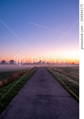 Summer Landscape with Field and Country Road Leading in the Fog. Dramatic Sky at Sunset Background Summer Landscape with Field and Country Road Leading in the Fog. Dramatic Sky at Sunset Background 104944175