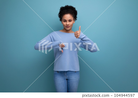 young curly brunette woman showing like and dislike on blue background with copy space 104944597