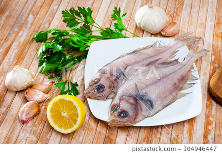 Uncooked roosterfish with greens and garlic on wooden board Uncooked roosterfish with greens and garlic on wooden board 104946447