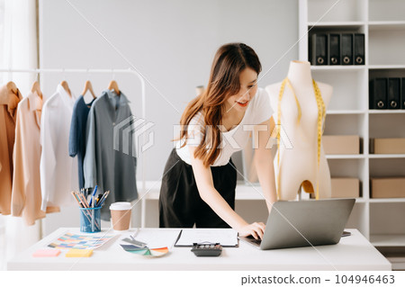 Asian tailor woman working on clothes in tailoring atelier. beautiful young female fashion designer smile and after success in modern studio Asian tailor woman working on clothes in tailoring atelier. beautiful young female fashion designer smile and after success in modern studio 104946463