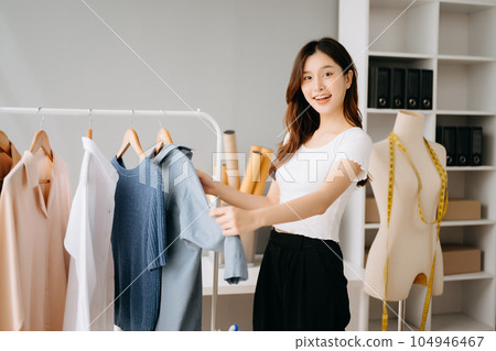 Asian tailor woman working on clothes in tailoring atelier. beautiful young female fashion designer smile and after success in modern studio Asian tailor woman working on clothes in tailoring atelier. beautiful young female fashion designer smile and after success in modern studio 104946467