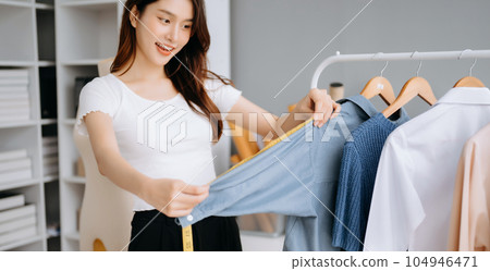 Asian young woman on desk in office of fashion designer and holds tablet, laptop and smartphone on white table Asian young woman on desk in office of fashion designer and holds tablet, laptop and smartphone on white table 104946471