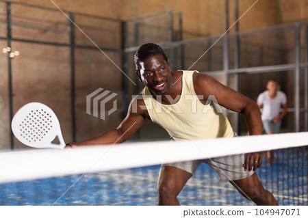 Expressive african american man playing paddle tennis on indoor court Expressive african american man playing paddle tennis on indoor court 104947071