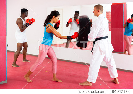 People in boxing gloves training punches in gym with trainer People in boxing gloves training punches in gym with trainer 104947124
