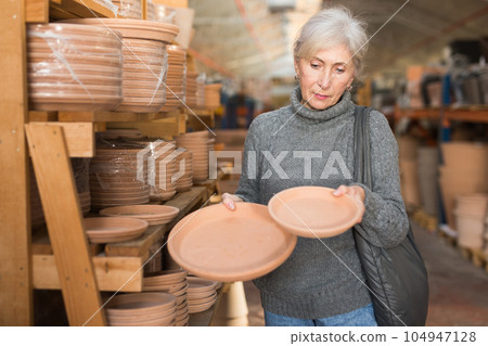 Eldrely woman selecting earthenware crockery in shop 104947128