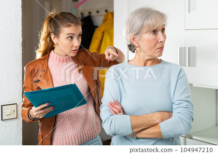 Female debt collector talking annoyed to worried elderly woman at home 104947210