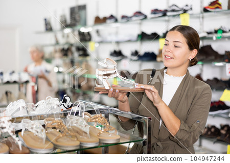 Girl client is demanding to inspect sandals in shoe showroom 104947244