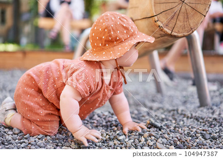 Cute child in panama. Crawling on all fours on pebbles. Portraits of a cute 10 months old baby girl. Walking on the playground, on a sunny summer day. 104947387