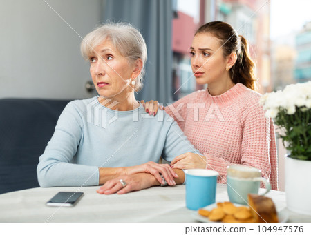 Girl asking for forgiveness from offended mother at home table 104947576