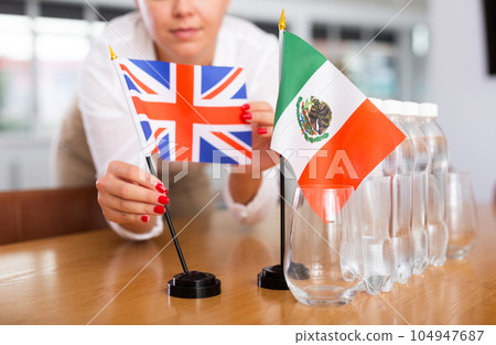 Unrecognizable girl sets midget flags of Mexico and Great Britain before international negotiations 104947687