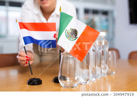 Unrecognizable girl sets midget flags of Mexico and Netherlands before international negotiations 104947919
