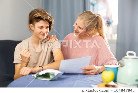 Happy woman with teenage son reading letter with good news 104947943