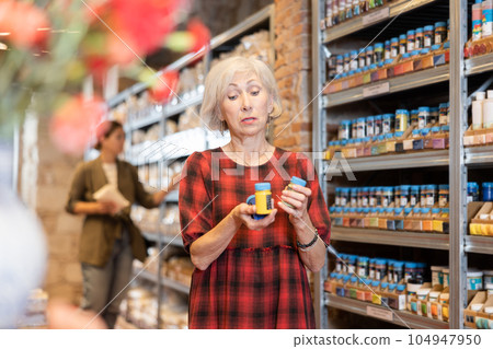 Elderly woman chooses multi-colored pigments for her future clay or ceramic dishes in specialized store 104947950