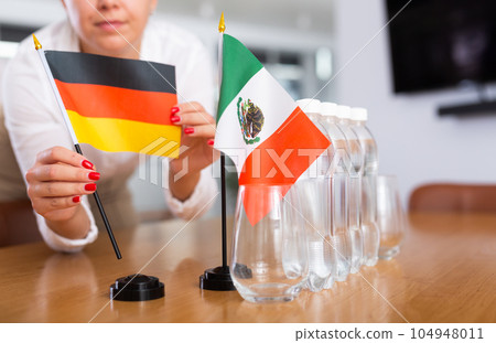 Unrecognizable girl sets midget flags of Mexico and Germany before international negotiations 104948011