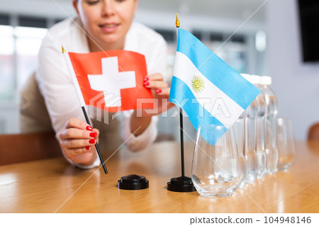 Little flag of Argentina on table and flag of Switzerland put next to it by young woman 104948146