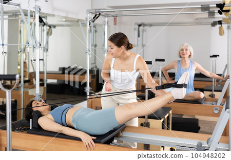 Young asian girl practicing pilates on reformer supervised by trainer 104948202
