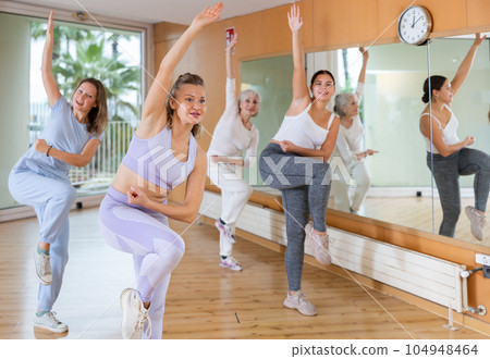 Group of excited young adult women in activewear performing dynamic movements during exercising together in fitness studio Group of excited young adult women in activewear performing dynamic movements during exercising together in fitness studio 104948464