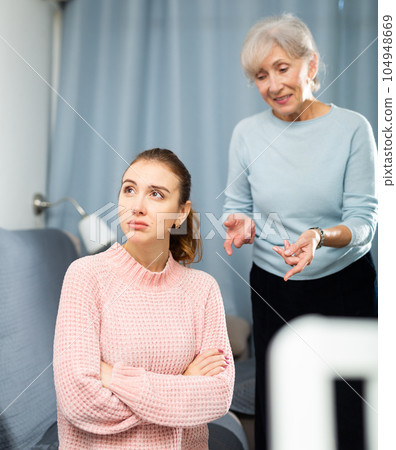 Upset young woman listening to reproaches from mother on sofa 104948669