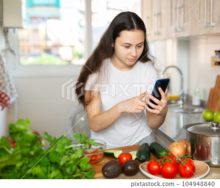 Woman using phone while making vegetable salad 104948840