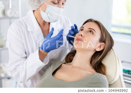 Beautician makeing cosmetic injection in the lips. Woman gets filler injection in her face. 104948992