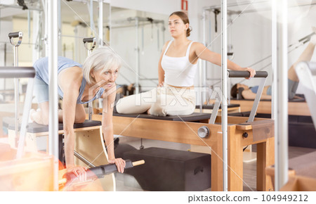 Mature woman practicing pilates stretching exercises on reformer at gym Mature woman practicing pilates stretching exercises on reformer at gym 104949212