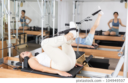 Side view of sports woman stretching body on pilates bed during workout Side view of sports woman stretching body on pilates bed during workout 104949507