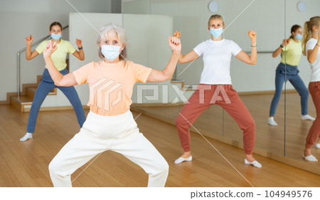 Female pensioner in mask exercising dance moves 104949576