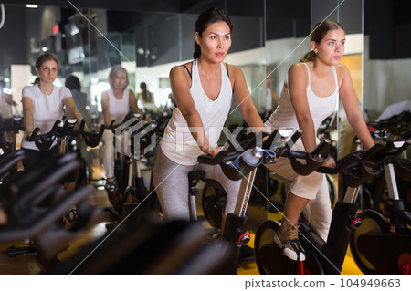 Women training on stationary bikes at gym 104949663