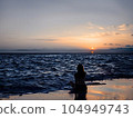 Silhouette of young woman sitting on the beach at sunset 104949743